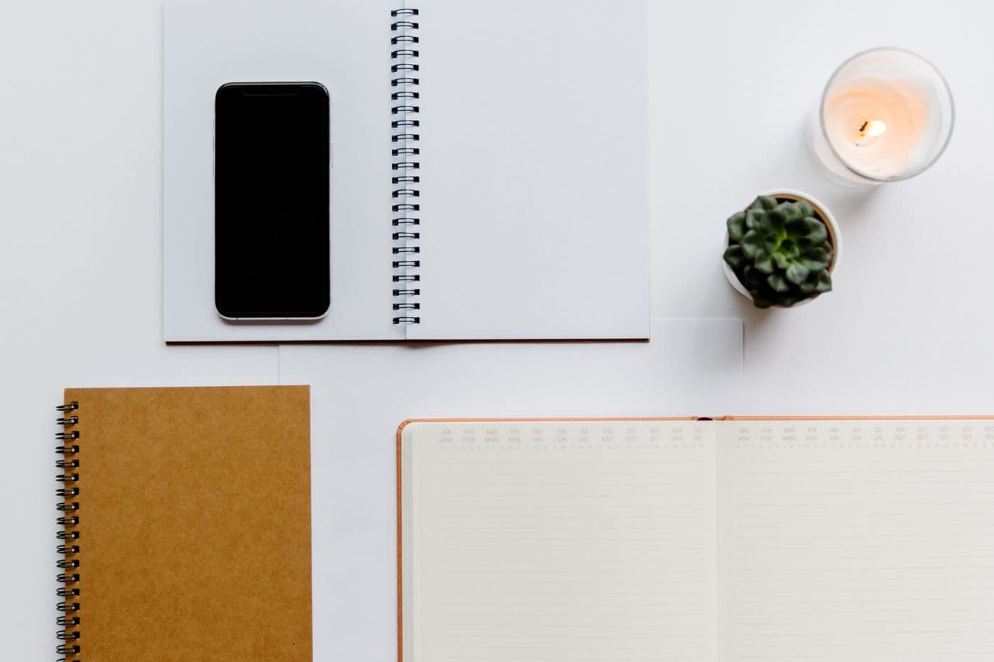 Desk flat lay with a notebook, phone and a small plant