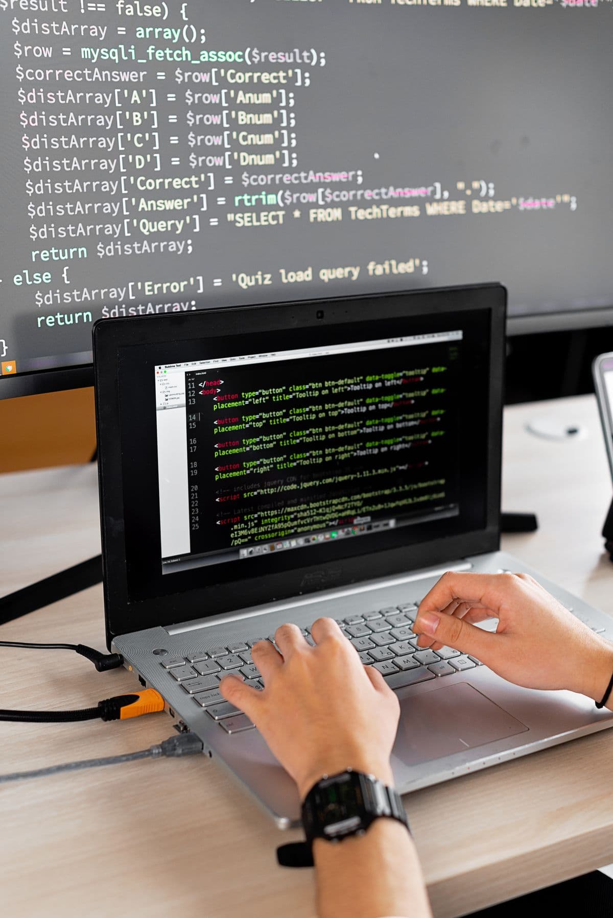 Developer writing PHP on a laptop with code on a second monitor